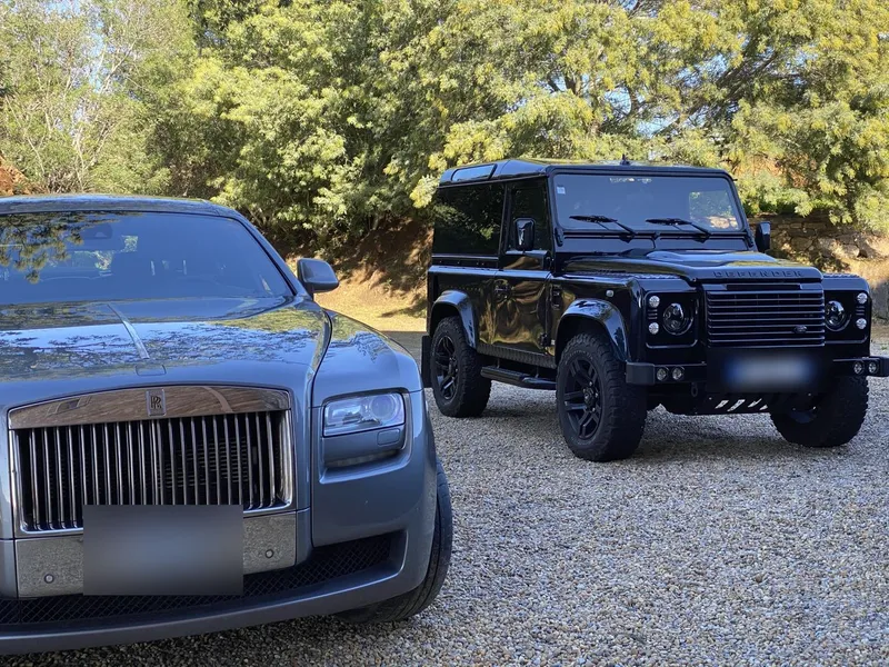 Une Rolls-Royce et le Defender garés sur du gravier, leurs deux plaques floutées.